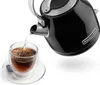 Hot water being poured from a black electric kettle into a clear glass teacup with a tea bag. Produktbild-Vorschau