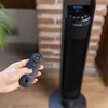 A hand holding a remote control is about to operate a black tower fan. Anteprima dell’immagine prodotto