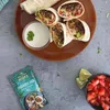 A plate of burritos with a side of dip and chopped tomatoes, next to a packet of burrito mix. Produktbild-Vorschau