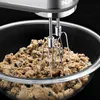 A close-up of a KitchenAid hand mixer mixing cookie dough in a glass bowl. Produktbild-Vorschau
