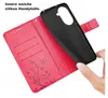 A hand is holding a black phone case over a red wallet-style phone case with card slots and floral/butterfly embossing. Produktbild-Vorschau