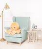 A plush octopus toy sits on a light blue armchair next to a small side table with a vase and an alarm clock. Anteprima dell’immagine prodotto