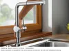 A hand is shown operating a kitchen faucet with a pull-out spray head, positioned next to a window. Náhled obrázku produktu