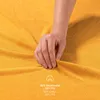A hand touching a yellow fabric, likely a bedsheet, with text indicating material composition. Anteprima dell’immagine prodotto