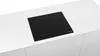 A black induction hob is installed on a white countertop. Produktbild-Vorschau