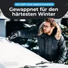 A man is scraping snow off a car windshield on a snowy day. Produktbild-Vorschau