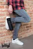 A person leaning against a brick wall, holding a black water bottle. Produktbild-Vorschau