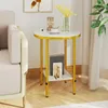 A small round side table with a marble-look top and gold legs, placed next to a sofa and a curtain. It has a shelf with books and a decorative item. Náhľad obrázku produktu