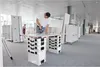 A man is assembling furniture in an office space with other furniture pieces in the background. Náhled obrázku produktu