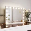 A vanity mirror with lights on a dresser, with flowers and jewelry in the foreground.