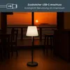 A floor lamp is placed in a room with a view of a sunset over the ocean. Produktbild-Vorschau