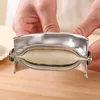 Hands are holding a stainless steel dumpling maker with dough inside, on a wooden surface. Produktbild-Vorschau