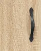 A close-up of a black cabinet handle on a wood-grain textured surface. Podgląd zdjęcia produktu