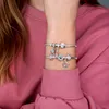 A close-up shot of a person's arm wearing two Pandora charm bracelets with various charms, including a horseshoe, hearts, and beads. Anteprima dell’immagine prodotto