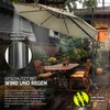 An outdoor patio scene with a large umbrella providing shade over a table and chairs, with rain falling. Anteprima dell’immagine prodotto