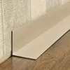 A close-up view of a beige L-shaped corner profile installed at the junction of a wall and a wooden floor. Produktbild-Vorschau