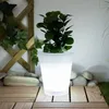 A lit planter with a plant sits on a wooden deck, surrounded by stones and a trellis with ivy. Produktbild-Vorschau