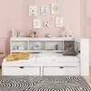 A white bed with drawers and a bookshelf headboard, set against a pink wall with framed pictures and decorations. Podgląd zdjęcia produktu