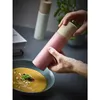 Hands holding a pink pepper mill over a bowl of soup. Produktbild-Vorschau