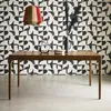 A wooden dining table with decorative items on it, set against a patterned wall. Produktbild-Vorschau