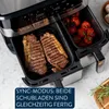 A close-up shot of a dual-chamber air fryer with steaks in one basket and tomatoes in the other, with text overlay. Produktbild-Vorschau