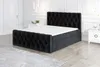 A black upholstered boxspring bed with a white mattress and topper, set in a well-lit, modern bedroom with white walls and doors. Produktbild-Vorschau