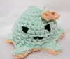 A crocheted stuffed toy with a face and a bow, resting on a fluffy white surface. Náhľad obrázku produktu