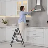 A woman is cleaning a kitchen range hood while standing on a step stool. Voir les images du produit