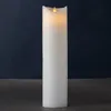 A tall, white LED candle with a flickering yellow flame sits on a dark surface against a dark blue background. Produktbild-Vorschau