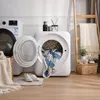 A laundry room scene with two dryers, one open with clothes inside, and a ladder with blankets. Produktbild-Vorschau