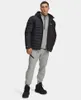 A man wearing a black puffer jacket and grey sweatpants stands against a white background. Náhled obrázku produktu