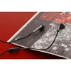 A pair of black Urbanista in-ear headphones with a microphone rests on a black and white magazine or book. Produktbild-Vorschau