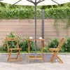 A wooden folding table and two chairs are set up on a patio under a large umbrella, with lush green foliage in the background. Produktbild-Vorschau