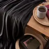 A dark gray blanket is draped over a wooden table, next to a mug of tea and a book. Anteprima dell’immagine prodotto