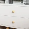Close-up of a white dresser with two wooden knobs, showing books and a mug on top. Podgląd zdjęcia produktu
