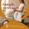 A woman is holding a white duvet in front of a washing machine, suggesting it is easy to clean. Voir les images du produit