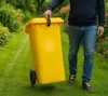 A person is walking a yellow trash can on a grassy path with flowers on either side. Produktbild-Vorschau