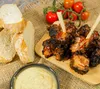 A close-up of grilled meat skewers with bread and dip, with tomatoes in the background. Náhľad obrázku produktu