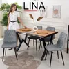 A woman stands by a dining table set with chairs, placemats, and a vase. Produktbild-Vorschau