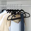 A close-up shot of several men's clothing items hanging on black velvet hangers from a closet rod. Anteprima dell’immagine prodotto