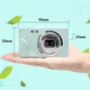 A hand holding a compact digital camera with dimensions indicated. Produktbild-Vorschau