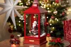 A festive Christmas scene with a red lantern containing a Santa Claus figurine and a Christmas tree, placed on a wooden table in front of a decorated Christmas tree. Produktbild-Vorschau