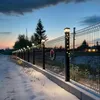 A fence decorated with Christmas lights and a wreath, in a snowy environment at dusk. Voir les images du produit