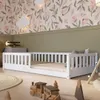 A child's bedroom with a white wooden bed, decorated with floral wallpaper and green wainscoting. Toys are scattered on the floor. Produktbild-Vorschau