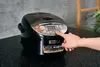 A person's hand is pressing a button on a black rice cooker. Produktbild-Vorschau