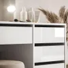A close-up view of a white dresser with a drawer and shelves, part of a vanity set. A makeup brush, cosmetic jars, and bottles are visible on the top surface. Produktbild-Vorschau