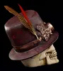 A steampunk-themed skull wearing a top hat, decorated with gears and feathers, against a black background. Produktbild-Vorschau