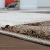A close-up, low-angle shot of the edge of a rug with a textured, patterned surface. Voir les images du produit