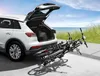 A white car with its trunk open, parked on a paved surface near a beach. Two bicycles are attached to a bike rack on the rear of the car, partially extending into the foreground. Produktbild-Vorschau