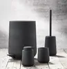 A set of black bathroom accessories, including a trash can, soap dispenser, toothbrush holder, and toilet brush, arranged on a wooden surface. Produktbild-Vorschau